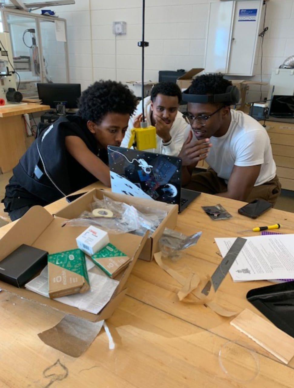 MKYF Three individuals engaged in a collaborative project at a workbench with various tools and components.